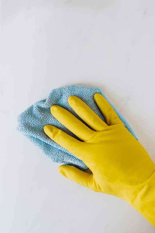 Person with a yellow rubber glove cleaning a marble counter